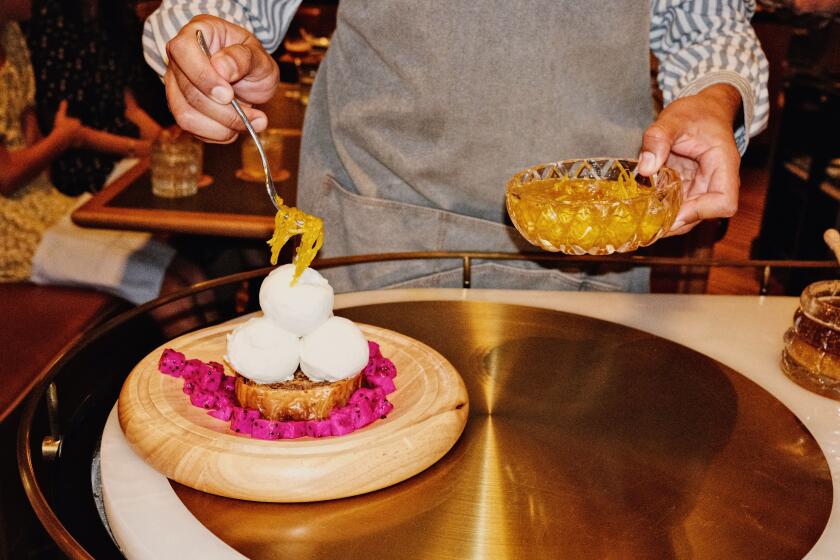 Hands spoon candied citrus on frozen Greek yogurt at a tableside dessert cart in Michael Mina's Orla in Santa Monica