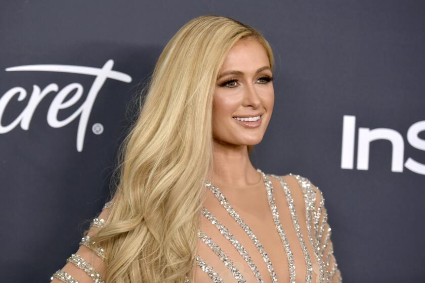 Paris Hilton smiling in a striped silver and nude dress