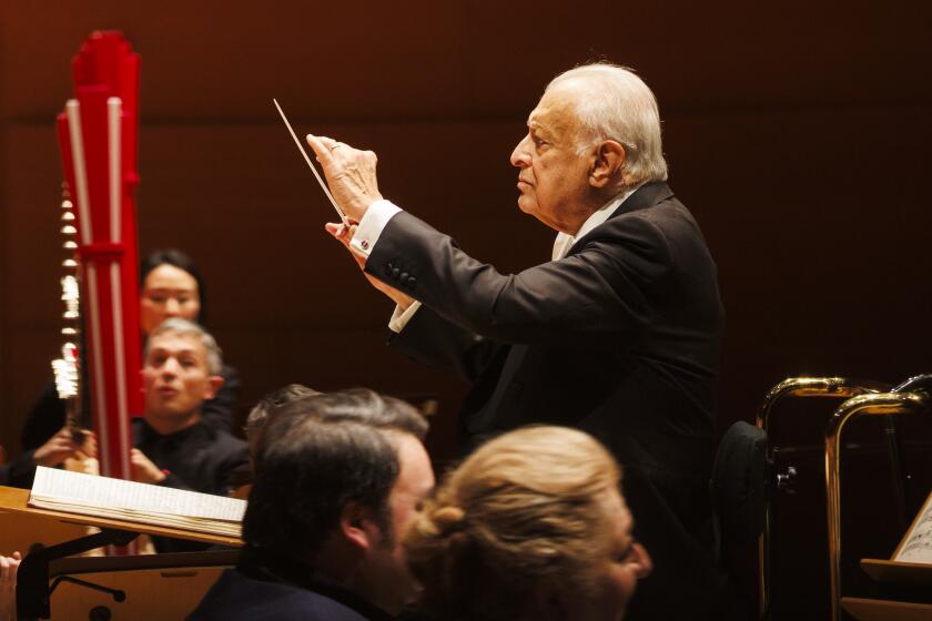 An 88-year-old conductor holds his baton as eyes of orchestra members wait for direction.