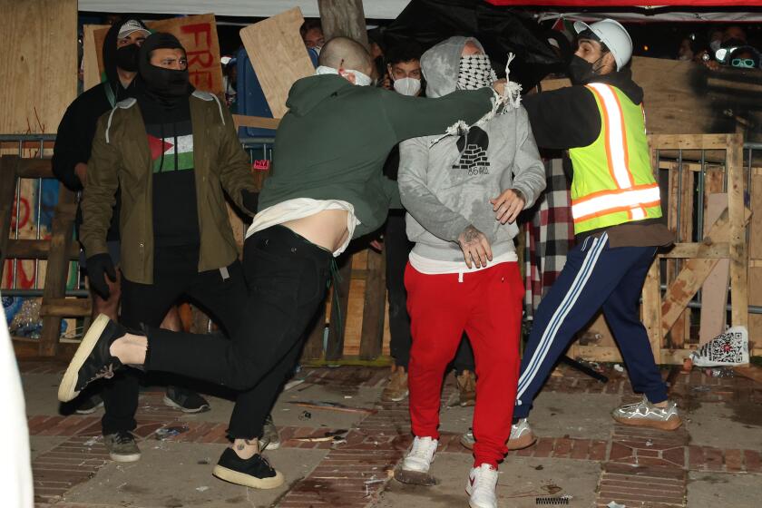 Los Angeles, CA - April 30: Barricades surround the encampment for the Pro-Palestine group as a member, right, is punched by a pro-Israel group member, left, at UCLA on Tuesday, April 30, 2024 in Los Angeles, CA. (Michael Blackshire / Los Angeles Times)