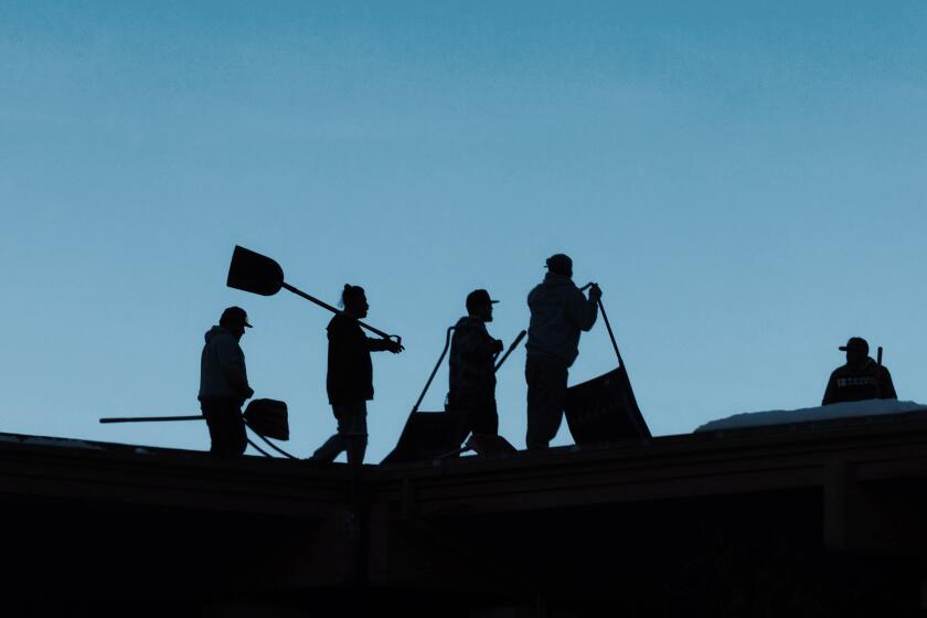 Mammoth Lakes, CA - December 03: Roofing company workers assemble to shovel snow off a building on Tuesday, Dec. 3, 2024 in Mammoth Lakes, CA. The threat of mass deportations in a town where most of the jobs are in hospitality and construction and half of the school kids come from Spanish speaking homes is concerning to many residents of the small Eastern Sierra town. (Brian van der Brug / Los Angeles Times)