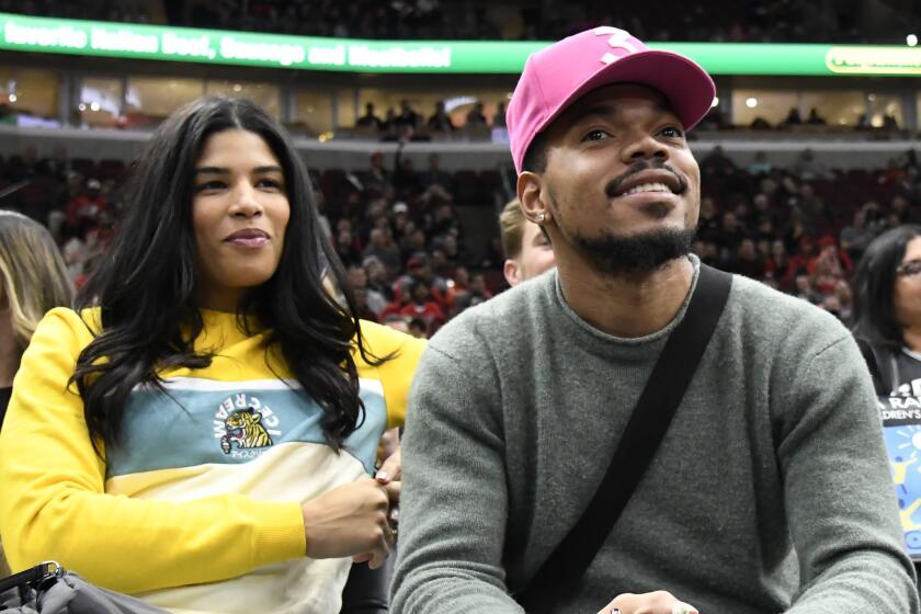 Kirsten Corley in a casual outfit sitting next to Chance the Rapper in a red hat and sweat shirt at a basketball game