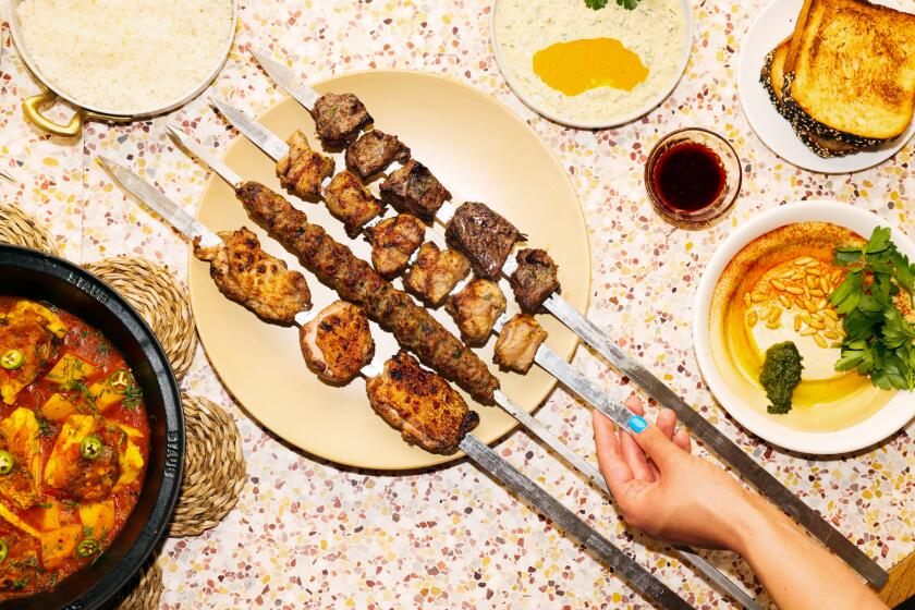 A hand grabbing a kebab in the middle of a spread of food.