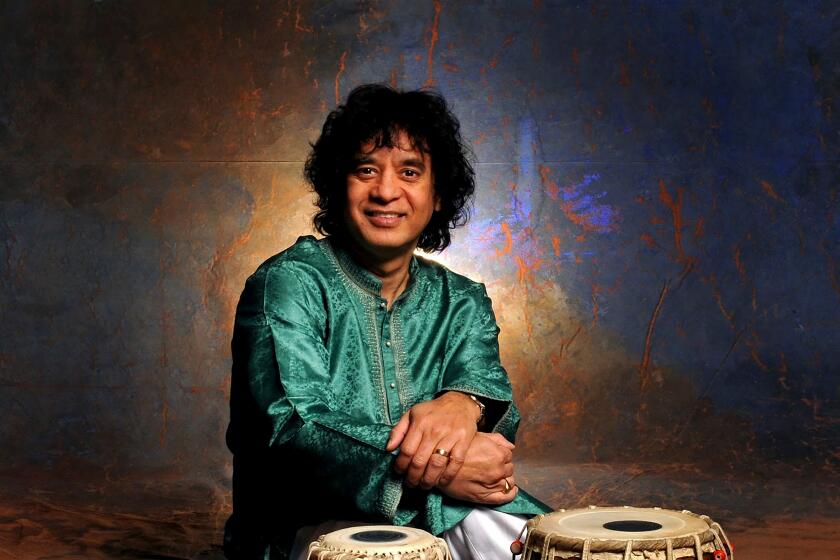 Zakir Hussain, in turquoise kurta, poses before tabla drum set