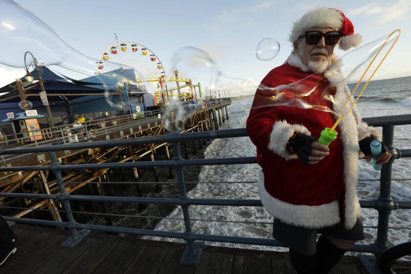 SANTA MONICA, CA - DECEMBER 24, 2021 - - Sid Lindenbaum, 78, dressed as Santa, blows bubbles on Christmas Eve on the Santa Monica Pier on December 24, 2021. He's been dressing like Santa and blowing bubbled on the Santa Monica Pier every Christmas Eve since 1995. He lives in Venice and is known as "The Venice Bubbleman." (Genaro Molina / Los Angeles Times)