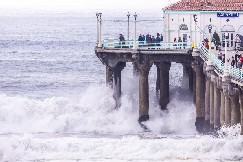 Manhattan Beach, CA - December 23: Visitors to Manhattan Beach Pier watch as waves crash under the pier during a high surf event on Monday, Dec. 23, 2024 in Manhattan Beach, CA. (Brian van der Brug / Los Angeles Times)